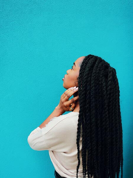 Black womxn with professional faux locs hairstyle standing with her back slightly to the camera, looking up