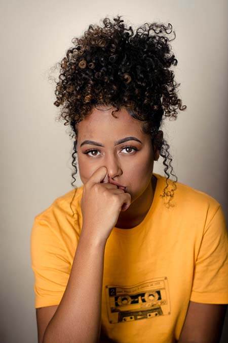 Black womxn with a professional natural twist curls hairstyle wearing a yellow t-shirt, sitting in front of a neutral background