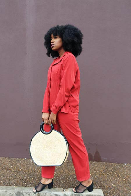 Black womxn with a professional 4C afro hairstyle standing on front of a purple wall, posing with a bag